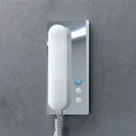 Speilblank dørtelefon med hvitt telefonrør og tre knapper.