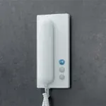 Hvit dørtelefon med tre knapper, montert på mørk vegg.