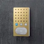 Gullfarget intercom med hvit høyttalerdel og tre knapper, montert på mørk vegg.