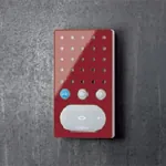 Rød intercom-enhet med hvit høyttalerdel og tre knapper, montert på mørk vegg.