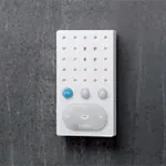 Hvit intercom-enhet med tre knapper og perforert høyttalergitter, montert på mørk vegg.