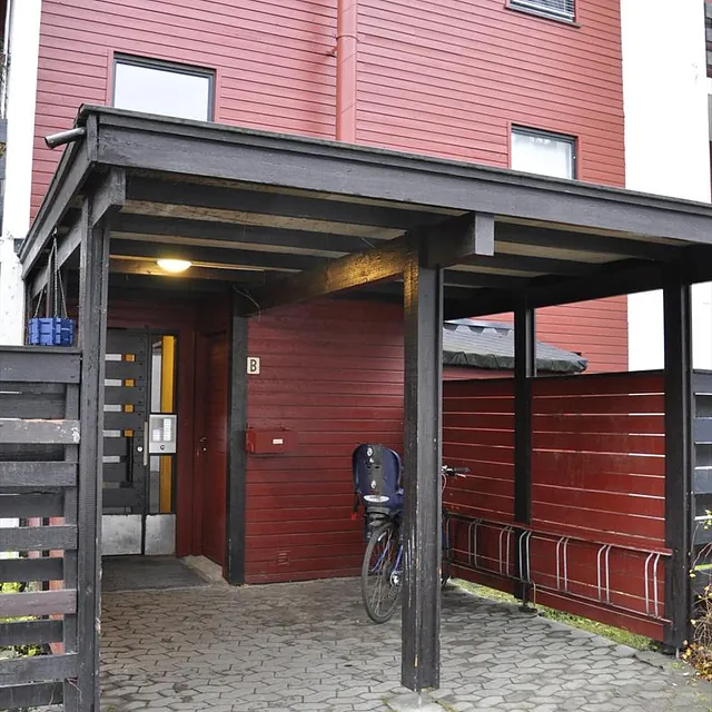 Inngangsparti med rød panelvegg, sykkelstativ og ringetablå ved dør merket med B.