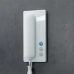 Hvit, blank dørtelefon med tre knapper og spiralkabel, på mørk bakgrunn.