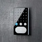 Sort intercom-enhet med blank overflate, hvit høyttalerdel og tre knapper, på mørk bakgrunn.
