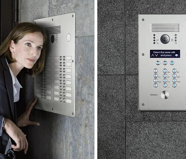 En kvinne bruker en stor dørtelefon med kamera og mange knapper på murvegg.