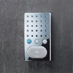 Speilblank intercom-enhet med tre knapper og hvit høyttalerdel, på mørk bakgrunn.