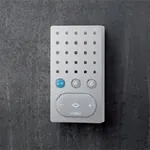 Børstet stål intercom med hvit høyttalerdel og tre knapper, montert på mørk bakgrunn.