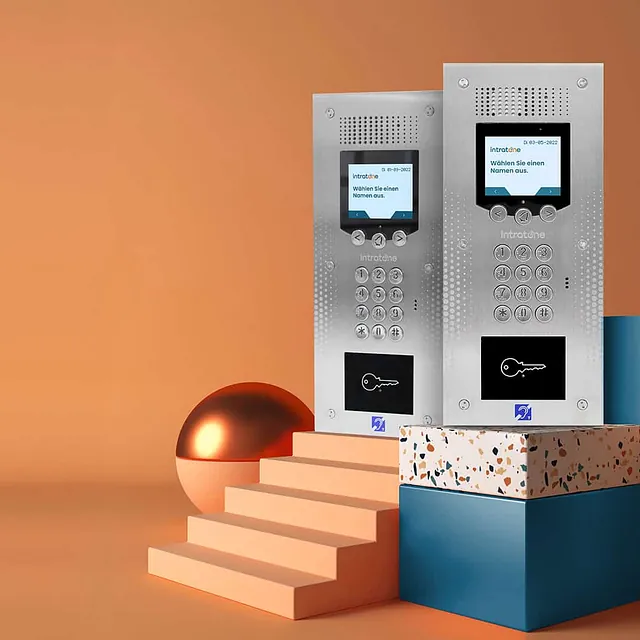 To porttelefonpaneler med skjerm, tastatur og kortleser står utstilt mot oransje bakgrunn.