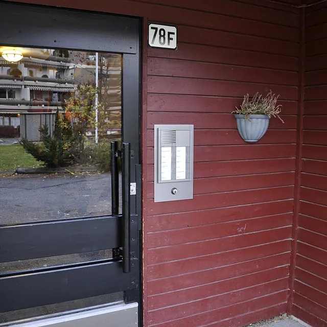 Inngangsdør med skilt 78F, ringetablå og blomsterpotte montert på rød trevegg.