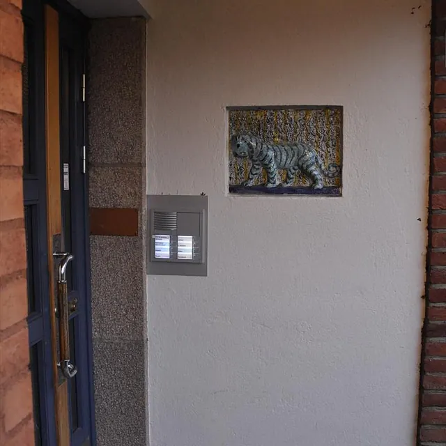 Ringetablå montert ved inngang med hvit vegg og dekorativt flisfelt med blå tiger.