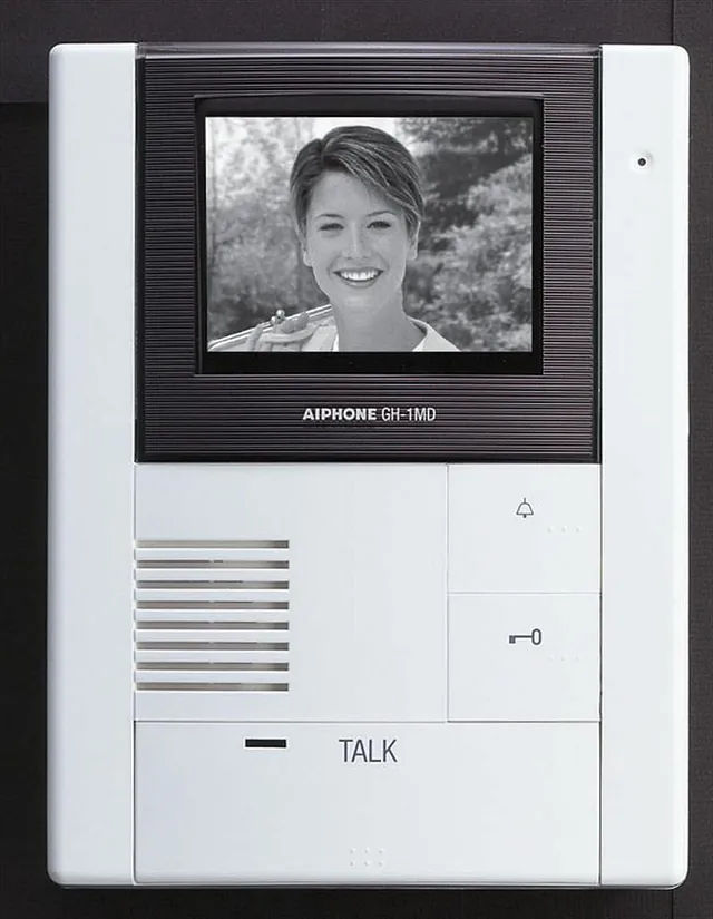 Hvit dørtelefon med stor skjerm, viser svart-hvitt-bilde av smilende kvinne.