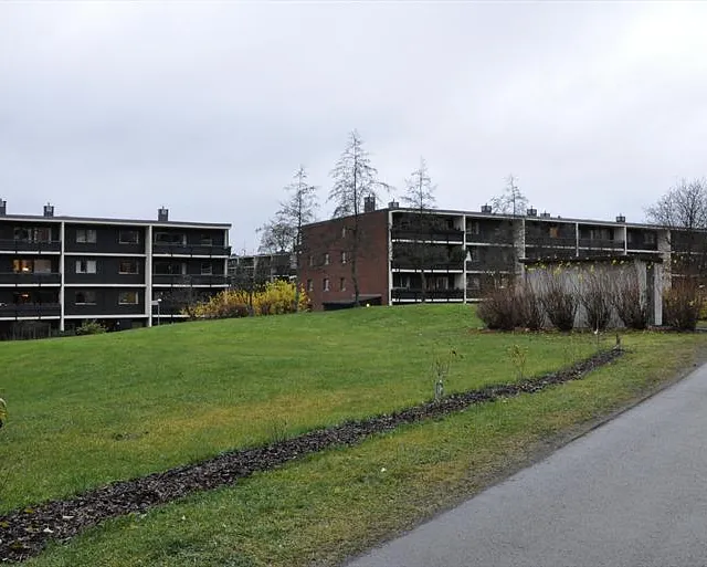 Tre lavblokker i mur og panel med store balkonger og plen foran, på en overskyet dag.
